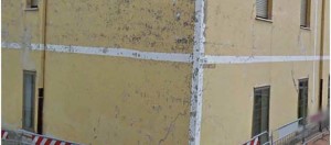 Abandoned building with severe structural damage and peeling yellow paint, marked with caution tape, highlighting safety concerns on the property.